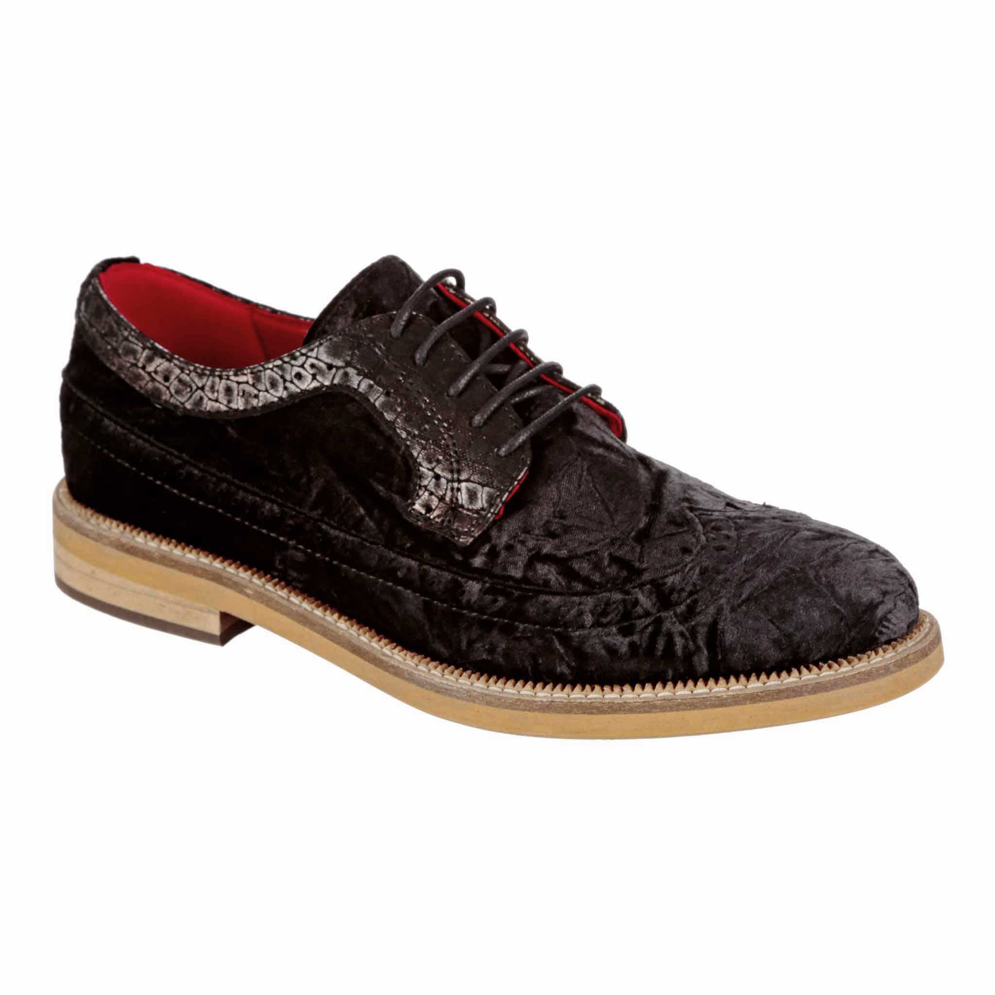 A black crushed velvet men's brogue shoe with red lining and brogue detailing, on a wooden effect sole.