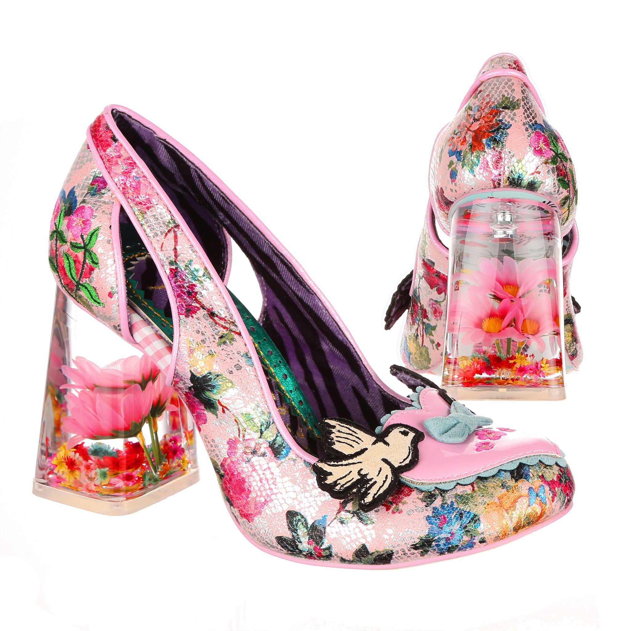 Pair of shoes with see through block high heels made of resin filled with dried and silk flowers.  The upper is made of pink metallic fabric with floral and snakeskin print, with a loveheart decal on the toe with two bluebirds. Paired shot, one at a side on angle, one from behind showing the heel design.