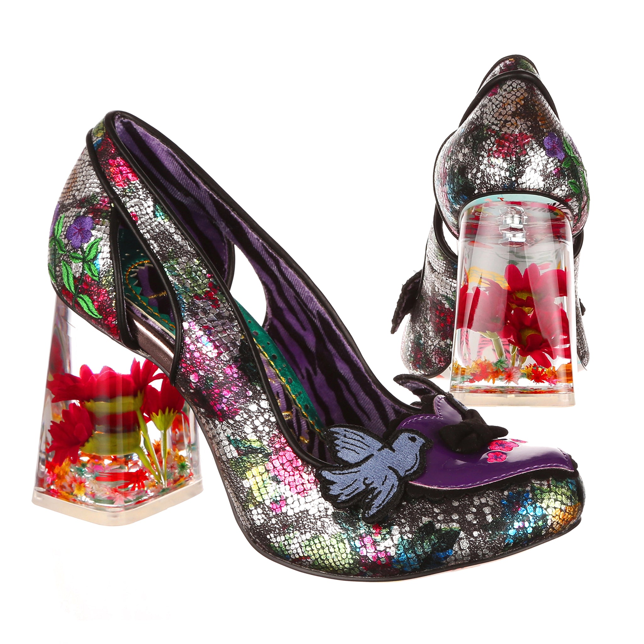 Pair of shoes with see through block high heels made of resin filled with dried and silk flowers.  The upper is made of black metallic fabric with floral and snakeskin print, with a loveheart decal on the toe with two bluebirds. Paired shot, one at a side on angle, one from behind showing the heel design.