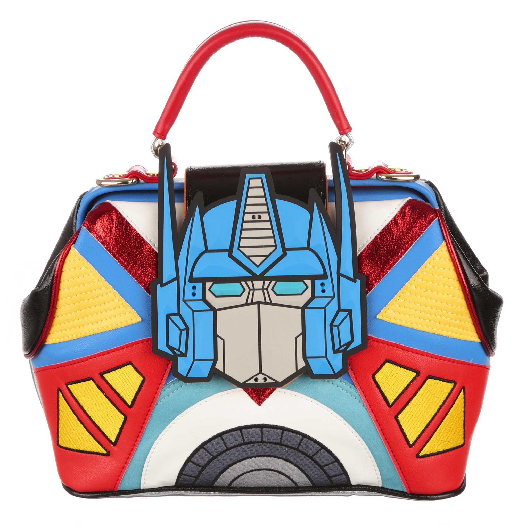 A multicoloured Transformers handbag, made up of blue, red, yellow and white geometric shapes decorated with embroidery stitching. A large blue Optimus Prime decal sits at the centre of the bag. A red handle with silver hardware clips sits at the top of Optimus Prime matching the red piping and completing the handbag.   