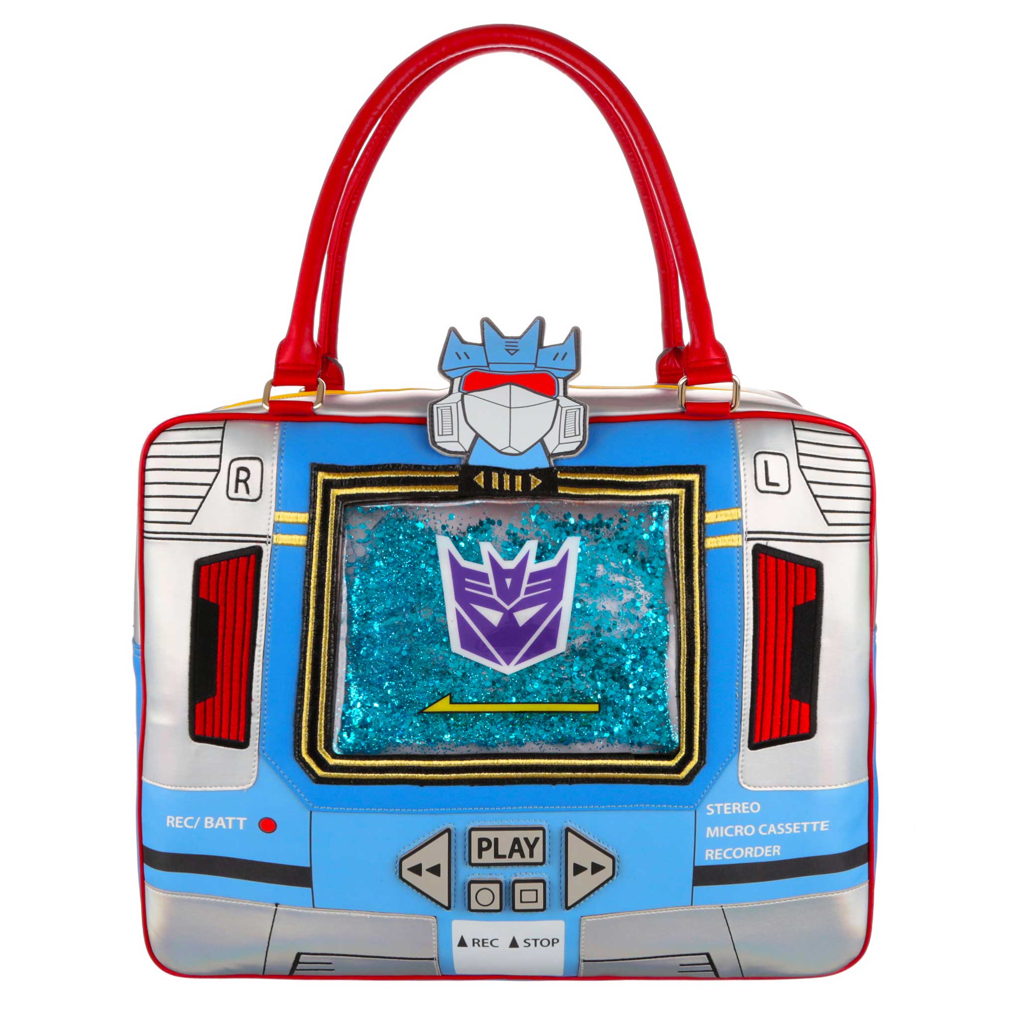 A large Transformers themed holdall in blue, silver and red. This rectangular shaped bag depicts the Transformer Soundwave robot with retro eighties cassette tape design details, it comes complete with play and stop buttons and on and off record buttons. A large blue glittering square sits on the centre of the bag where the tape deck would be with a purple Decepticon logo on it. Soundwave’s face sits at the top of the bag with a large red structured handle arching over the top of the handbag. 
